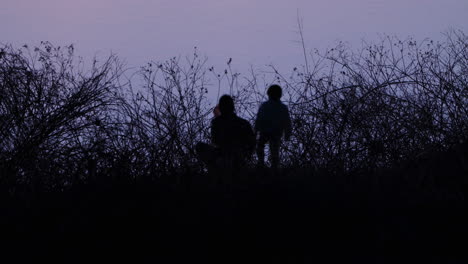 silhouetted image of father and son fishing with a net on the river at dusk in tokyo, japan