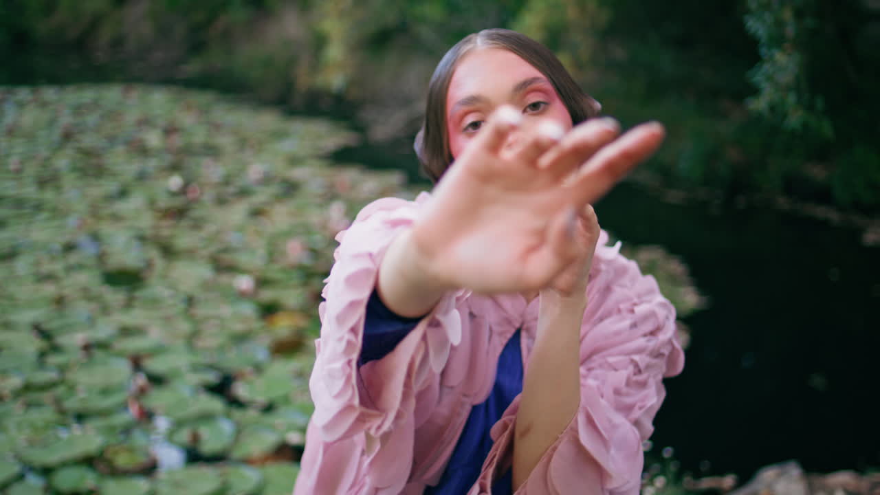 미스터리한 소녀가 카메라로 포즈를 취하고 공원 연못에 손을 흔들고 있다.