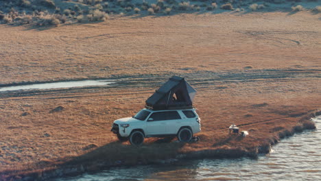 Wild-off-grid-campsite-on-shore-of-fresh-water-lake,-Roofnest-tent-on-car,-aerial