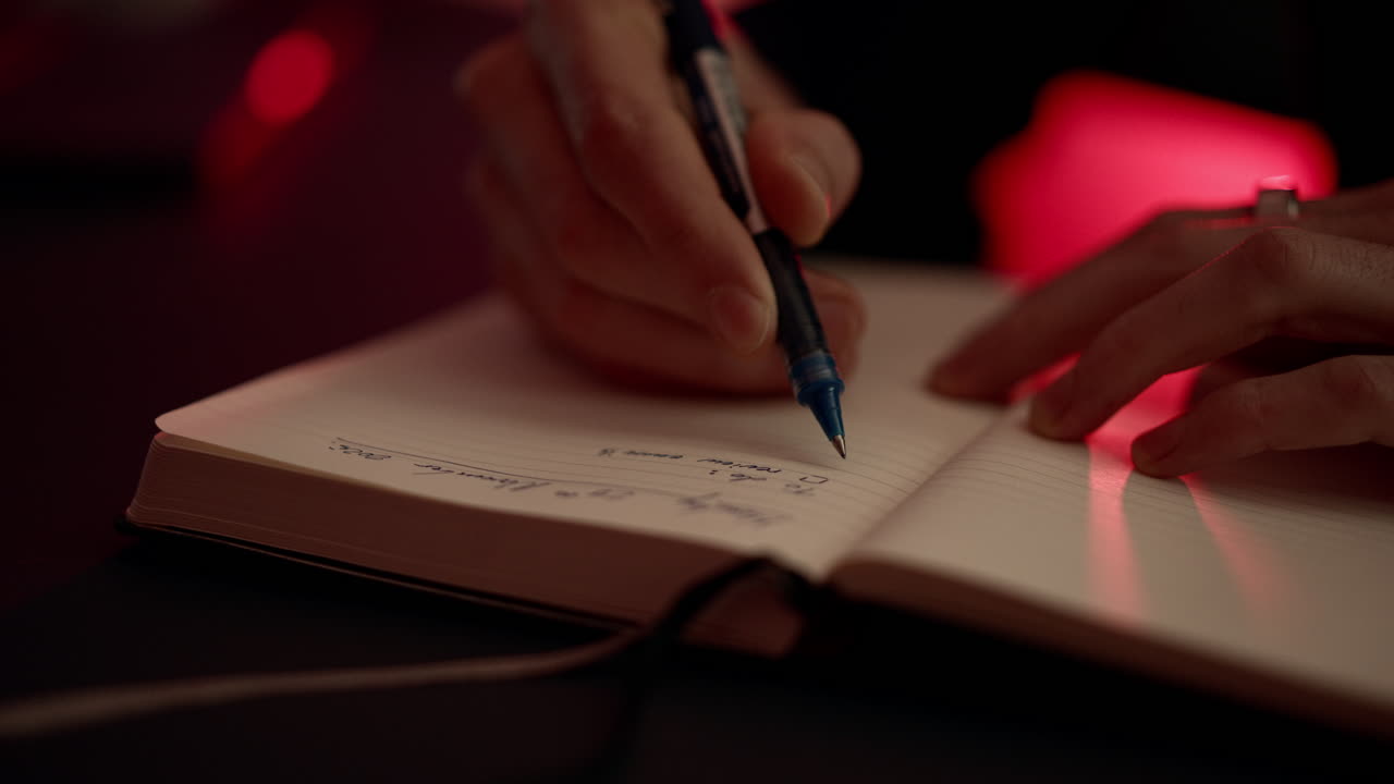 Close-up of a hand writing in a notebook under warm, moody lighting. Creative, focused moment capturing journaling, planning, and personal reflection in a cozy cinematic setting