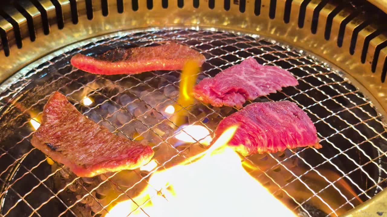 Primo piano di carne di manzo cruda marmorizzata che cuoce su una griglia a carbone con fiamme arancioni tremolanti.