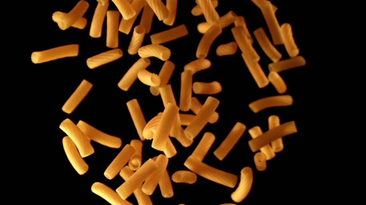 Pasta maccheroni secca che cade al rallentatore su sfondo nero.