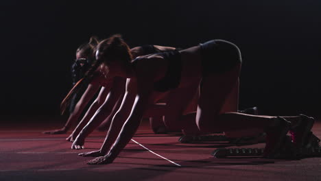 three girls in black clothes are in the starting pads to start the race in the competition in the light of the lights and run towards the finish