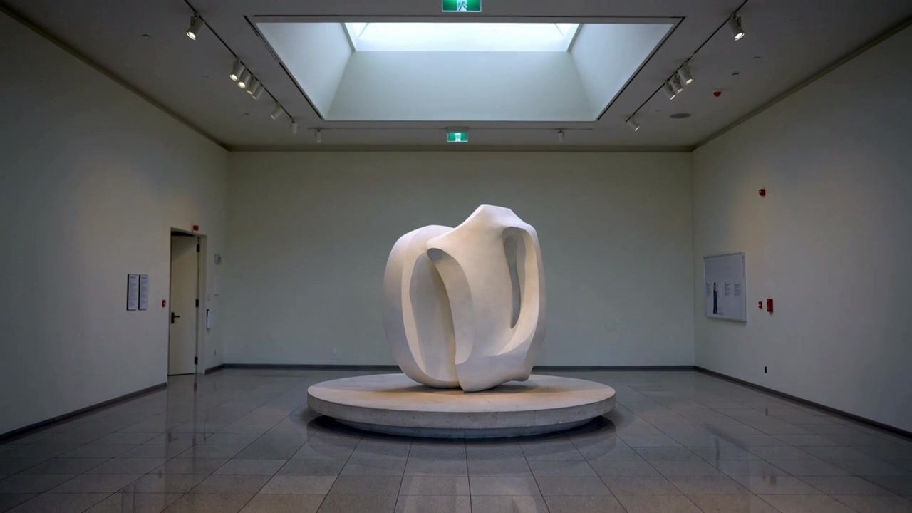Kamera trekker seg tilbake og avslører et galleri for å vise skalaen av en sentrert abstrakt skulptur på en sokkel.
