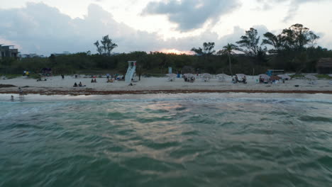 Drone-Volando-Sobre-La-Superficie-Del-Agua-Hacia-La-Playa-De-Arena.-Tiro-Ascendente-Que-Revela-La-Ciudad-De-Playa-Del-Carmen,-México