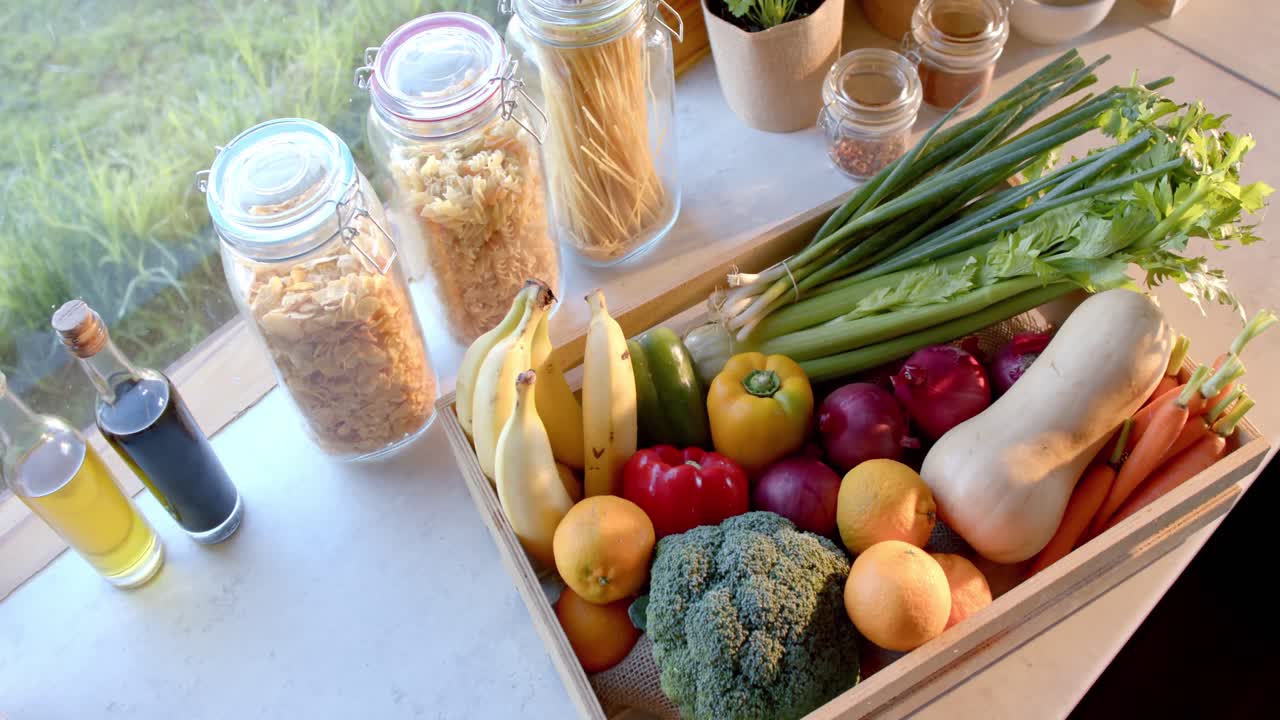 caja de verduras orgánicas y frascos de almacenamiento de alimentos en la encimera en la cocina soleada, cámara lenta