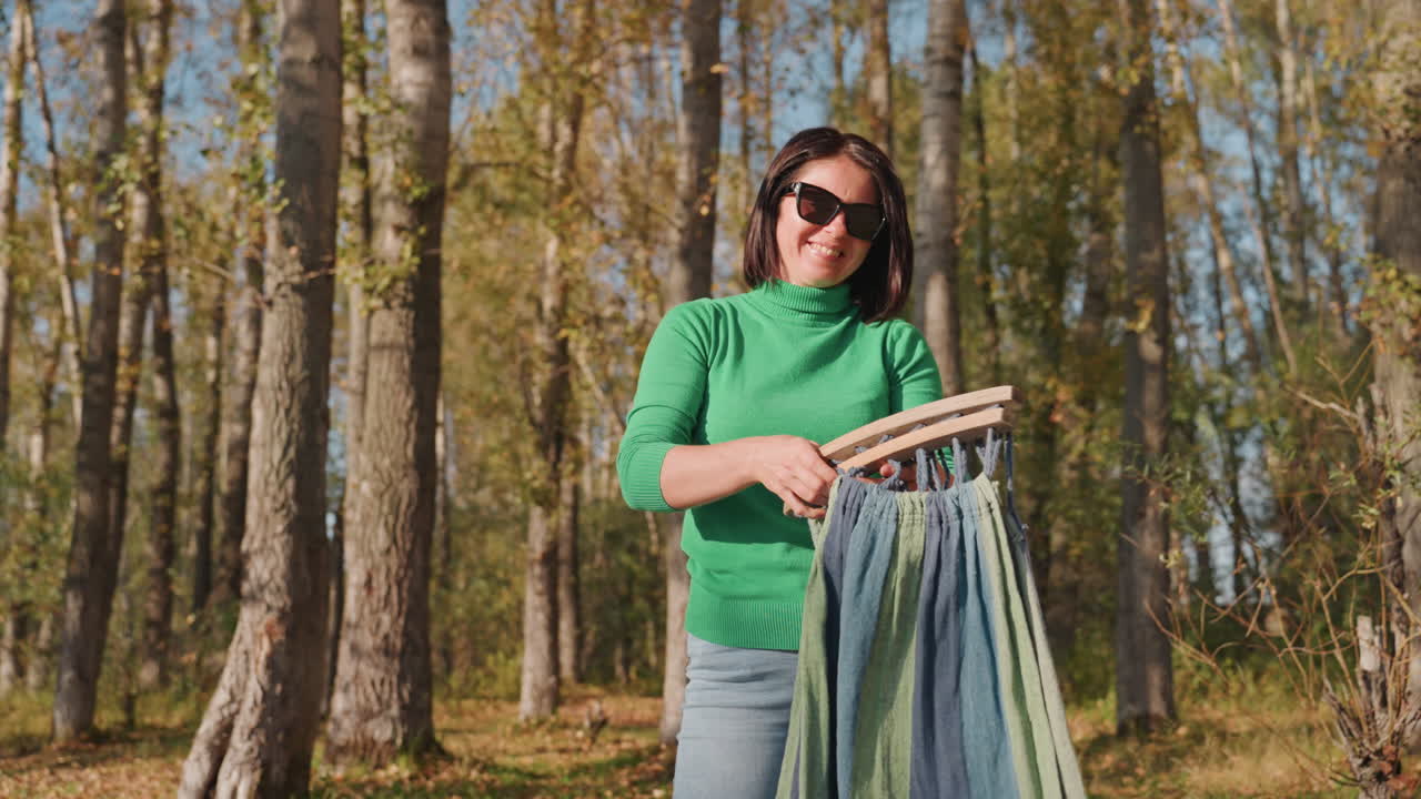 Scena all'aperto con donna e amaca. Donna sorridente mentre prepara e sistema l'amaca all'aperto in un boschetto. Donna allegra che srotola e fissa un'amaca intrecciata sotto gli alberi durante un campeggio all'aperto.