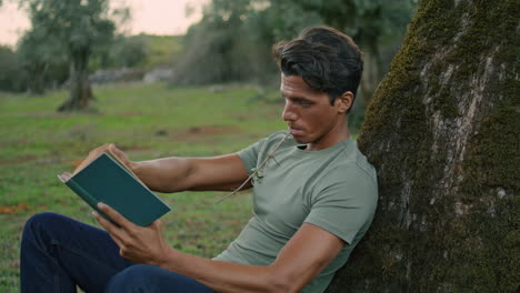 focused man flipping book evening park closeup. guy reading literature at nature
