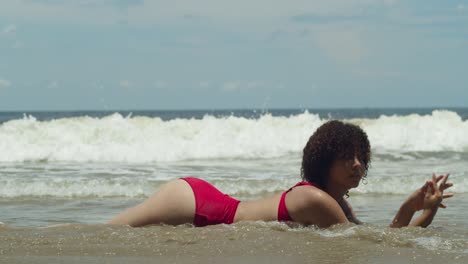 una joven vestida de bikini rojo con cabello rizado ilumina una isla tropical en un día soleado en la costa con olas del océano en el fondo