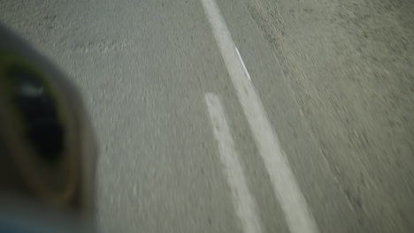 a motion blur view of a tarred road with visible white lane markings, slight reflection from an object nearby is seen on the side