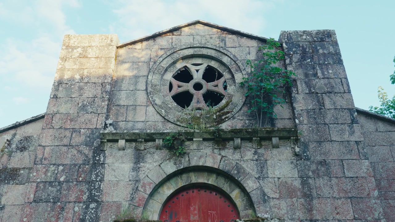 Chiesa in pietra invecchiata con accenti verdi e una grande finestra circolare, sullo sfondo di un cielo azzurro tenue