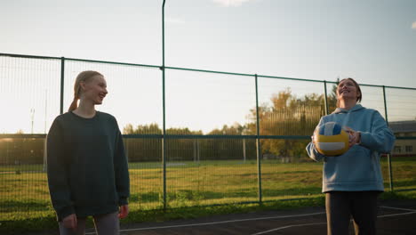 smiling volleyball beginner practicing how to play volleyball outdoors with sunlight glowing in background, young athlete learning and enjoying volleyball practice on court with green field behind