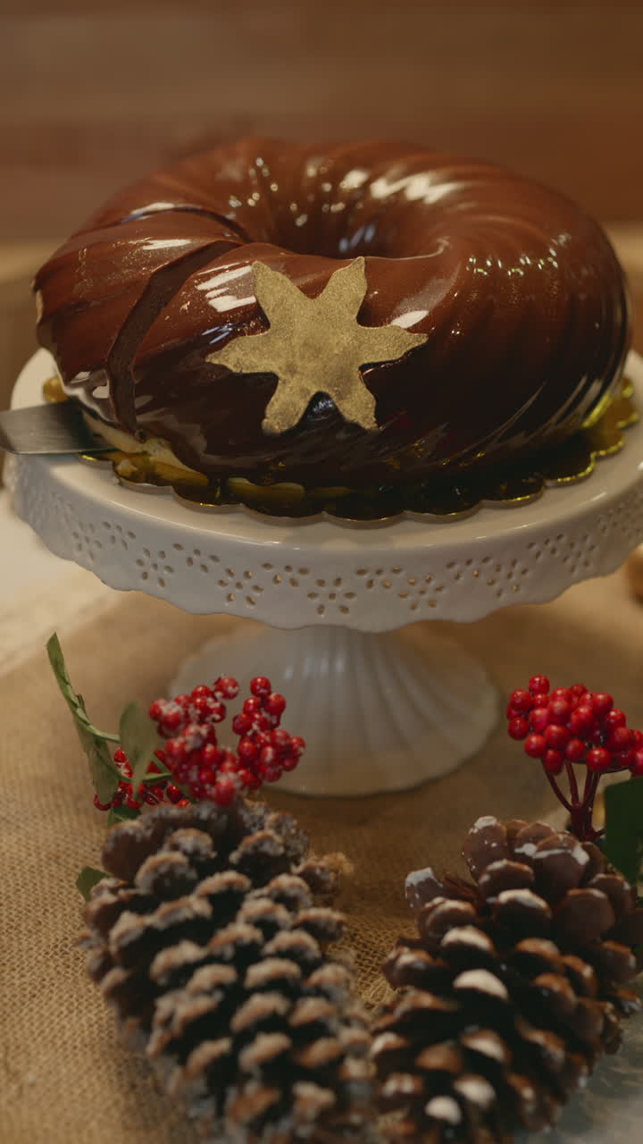 Close-up clip of a Christmas dessert covered in shiny chocolate frosting and decorated with a gold star. Presented on a white pedestal