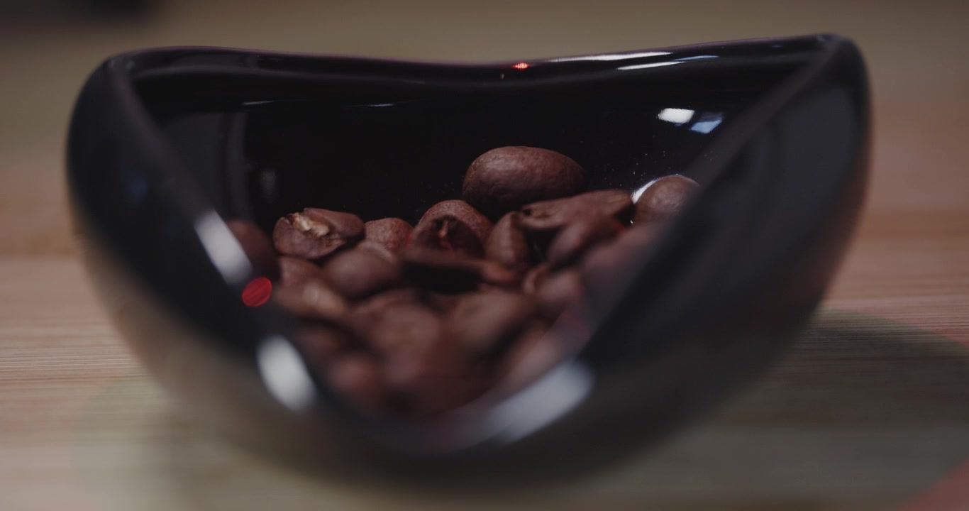 Ripresa al rallentatore di chicchi di caffè appena tostati che cadono in una tazza dosatrice per caffè sopra altri chicchi.