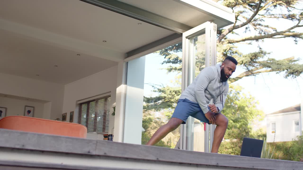hombre afroamericano centrado en el entrenamiento físico estirándose en la cubierta en el jardín soleado, cámara lenta
