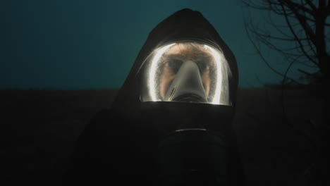man with gas mask at night looks into the woods