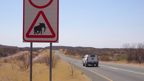 a beware of elephant crossing sign with jeep passing warns visitors on a dirt road in namibia africa