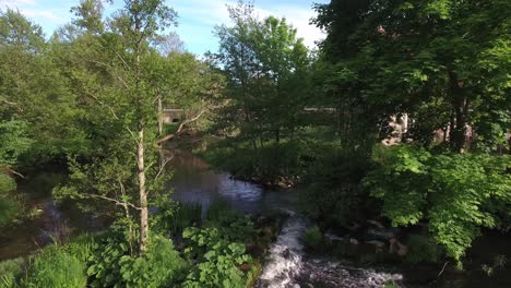 Fliegen-über-Kleine-Brücke-Und-Durch-Bäume-An-Einem-Ruhigen-Kleinen-Fluss-Im-Sommer-In-Südschweden-Skåne,-österlen-Nybroån,-Luft-Langsam-Vorwärts