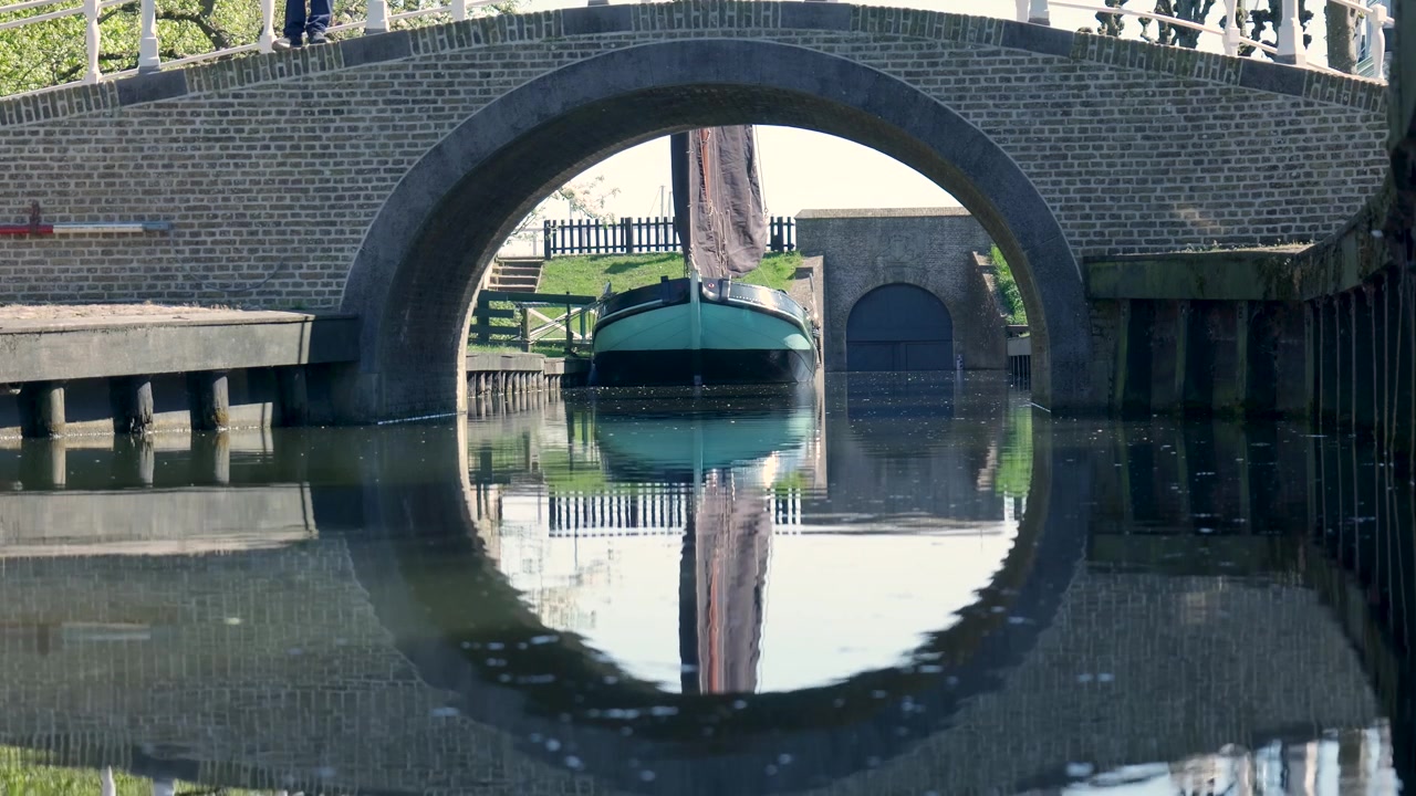 Pequeña embarcación amarrada bajo un puente de arco de ladrillo en un canal