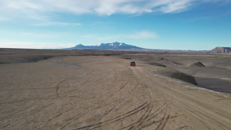 Red-Van-Moving-on-Dirt-Road-in-Desert-Landscape,-Tracking-Drone-Shot