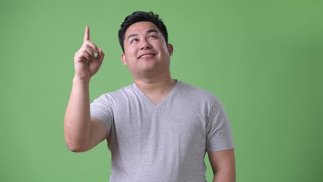 young handsome overweight asian man against green background