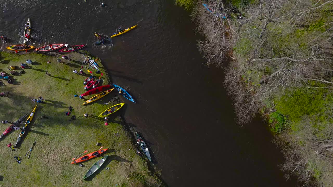Top down aerial view of kayaks paddling below rapid on river while paddle boats flips over, capsizes after going through a rapids. People on riverbank shore and paddlers resting, Võhandu row marathon