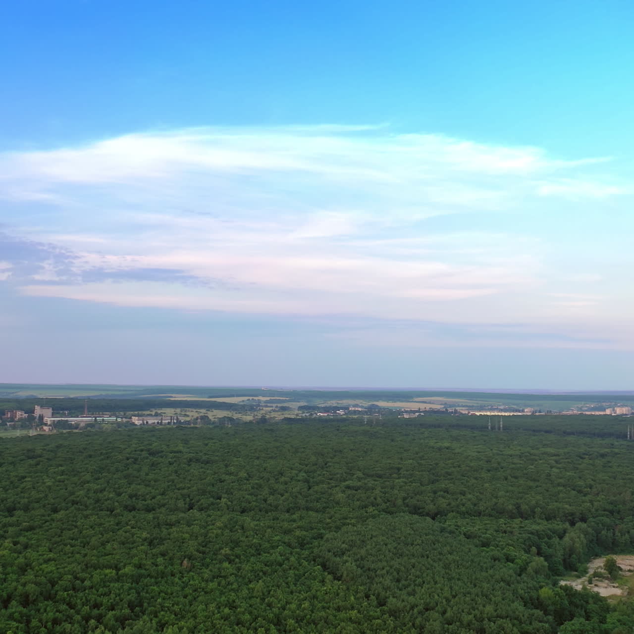 Drone is rising up over the natural environment in summer. Green forest under bright sky outdoors. Beautiful scenery in the countryside.