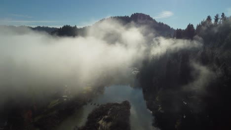 Aéreo:-Volando-A-Través-De-Nubes-Bajas-Sobre-El-Río-Y-La-Pequeña-Ciudad