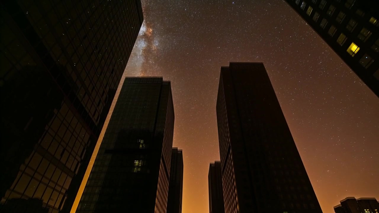 Telecamera che inquadra una strada con torri di vetro, con il tramonto che si intensifica e rivela finestre e la Via Lattea.