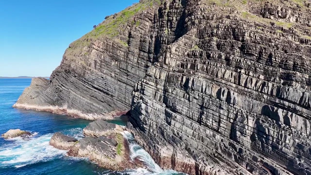 Drohnenaufnahme von geschichteten Sedimentklippen und blauen Meereswellen bei Crescent Head, Australien