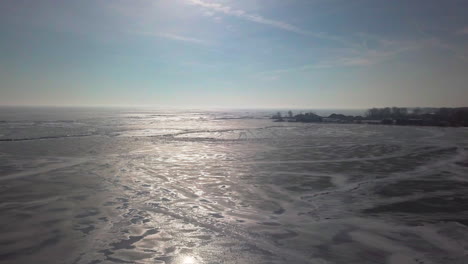 drone flys forward and down towards the frozen lake with a boat and dock in the distance