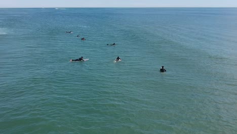 Drone-Flyover-Group-of-Surfers-Waiting-to-Catch-Waves-All-Wearing-Black-Wetsuits