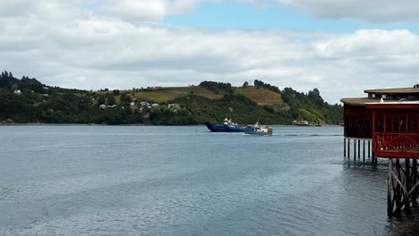 Tranquil-scene-of-Dalcahue-waterfront,-Boat-sailing-along-shore,-Pan-shot