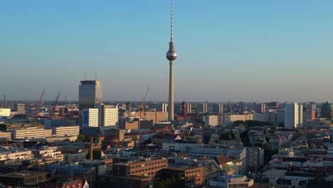 berlin tv tower standing tall over the tower and red town hall, bathed in the warm glow of golden hour. stunning aerial view flight wide orbit overview drone