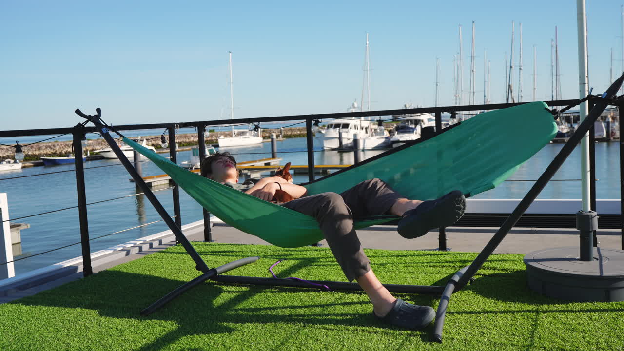 Jovem e cão relaxando em rede na marina