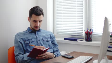 joven empresario sentado junto a la computadora en una elegante oficina moderna y tomando notas usando su lápiz y cuaderno. computadora