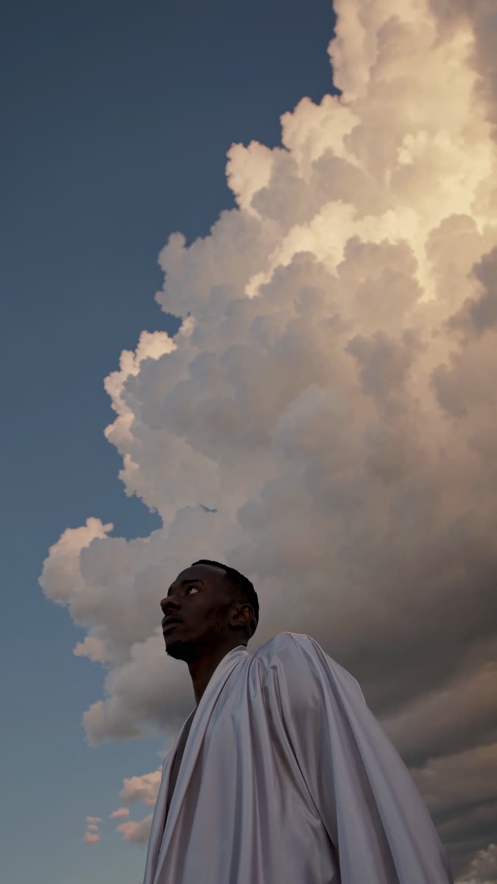 A dramatic low-angle video shot of a person in white against towering clouds, emphasizing grandeur