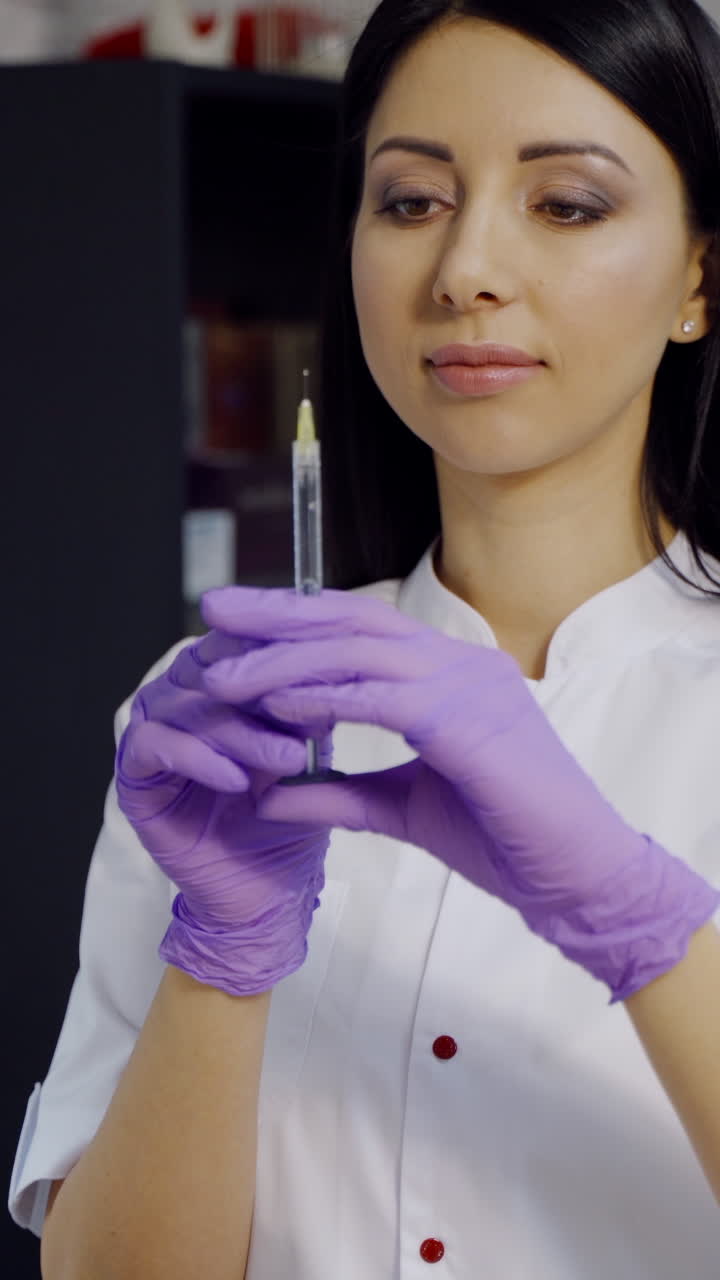 Cute cosmetologist with long hair checks a syringe before the Botox procedure in the office on the background of a cupboard in a beauty salon. Vertical video
