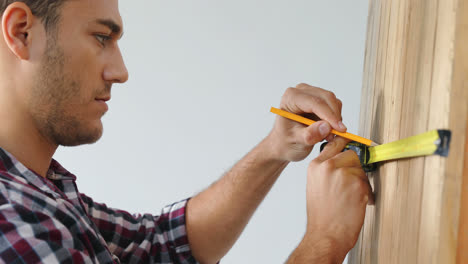 Smiling-male-architect-measuring-wall-with-measuring-tape-against-white-background-4K-4k