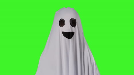 child dressed up in ghost costume knocking on door trick or treating at halloween with pumpkin shaped jack o'lantern bucket against studio green screen