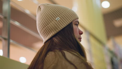 close-up side profile of a young girl wearing a brown ribbed beanie, with long hair resting on her shoulder. contemplative moment, with soft indoor lighting creating a warm atmosphere. blur background