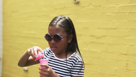 en un patio de escuela, una joven de dos razas soplando burbujas, fondo amarillo