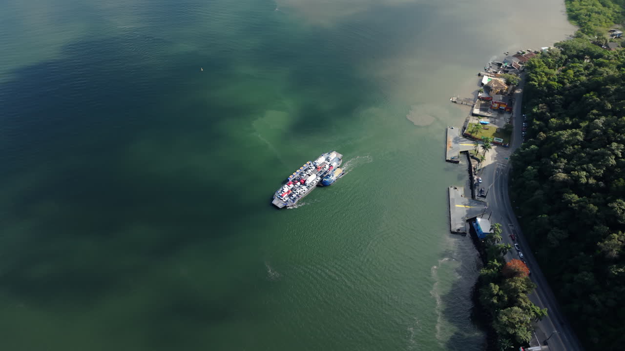 Drone capture over a ferry boat moving through greenish coastal waters near a forested shoreline, Guaratuba, Paraná, Brazil