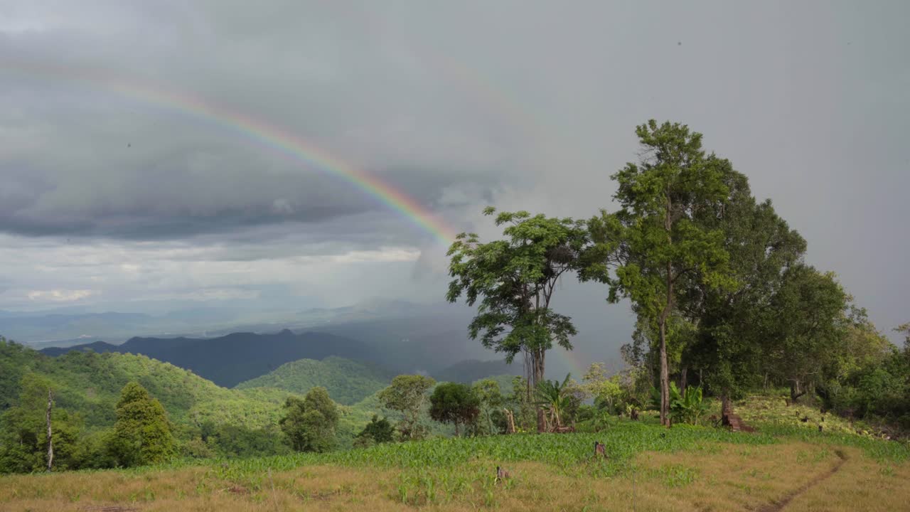 vista cinematográfica en 4k desde la cima de una montaña iluminada por el sol en mae tang, tailandia, mostrando un arco iris vibrante y expansivo sobre picos iluminados por el sol
