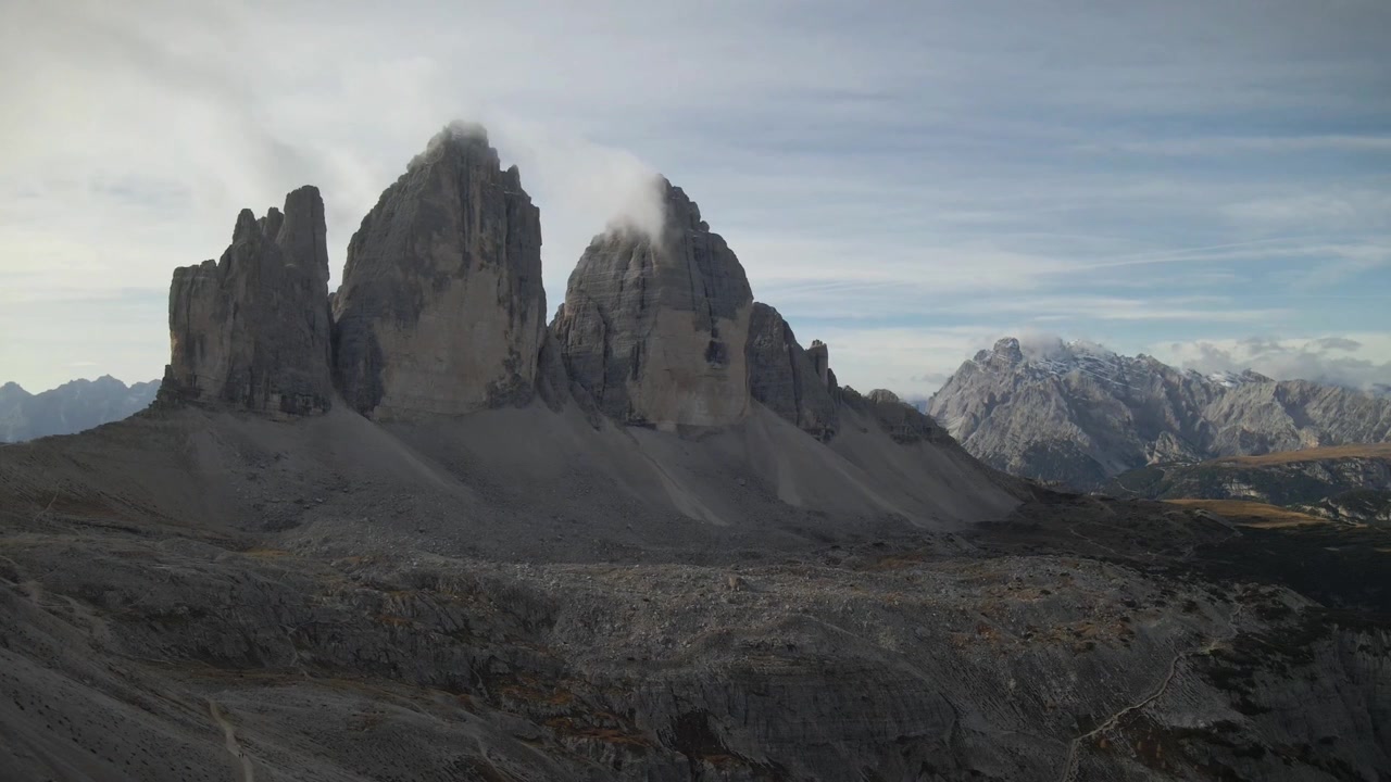 Vue imprenable sur les Drei Zinnen, sommets emblématiques du Tyrol du Sud, Italie, entourés d'un terrain accidenté et d'un paysage alpin, sous un ciel bleu serein avec de doux nuages
