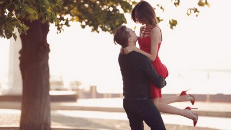 young guy holds a girl and circles her. romantic and loving couple at sunset