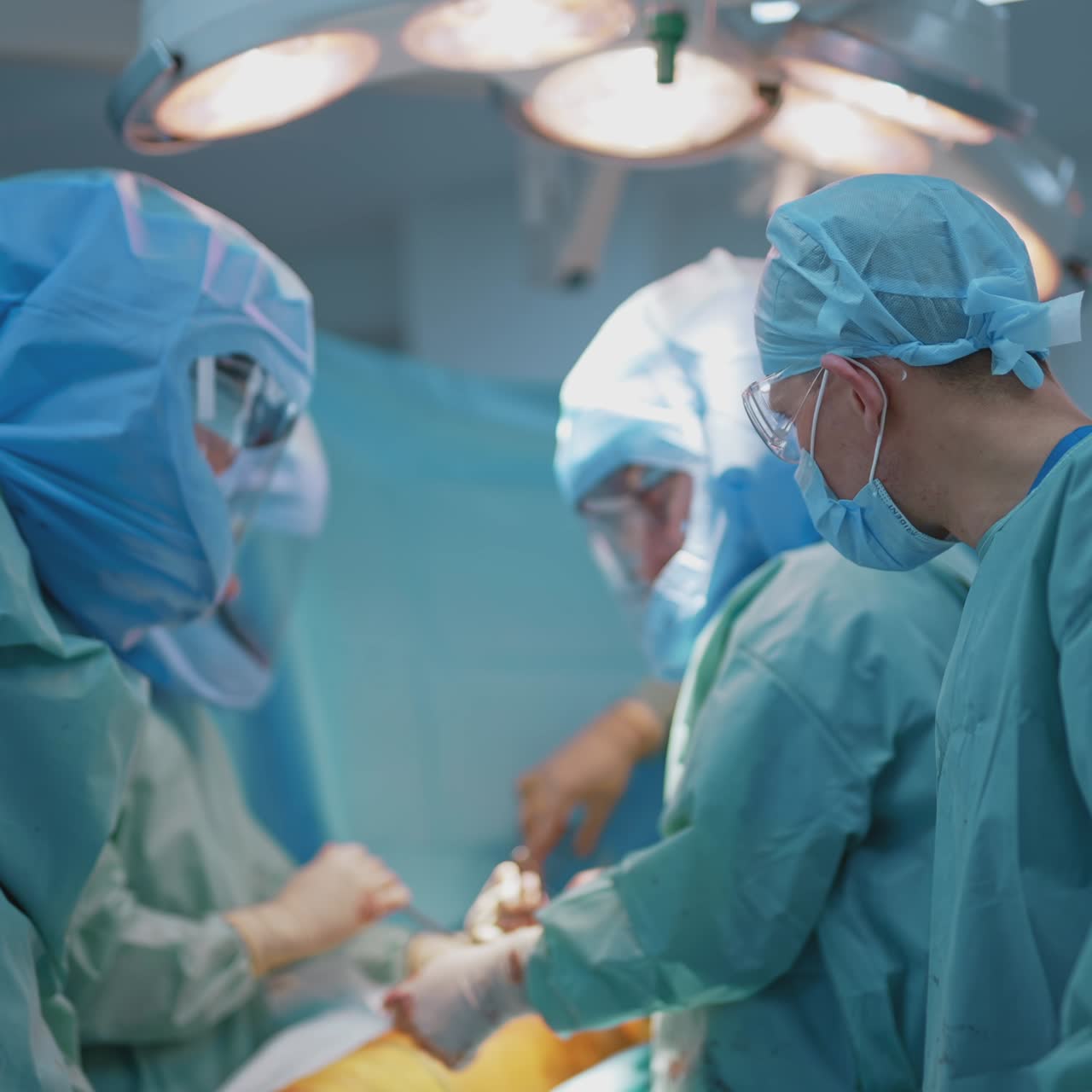 Team of surgeons operating infected patient. Group of doctors in safety suits working in the operating room. Male assistant in mask help medical specialists. Covid 19
