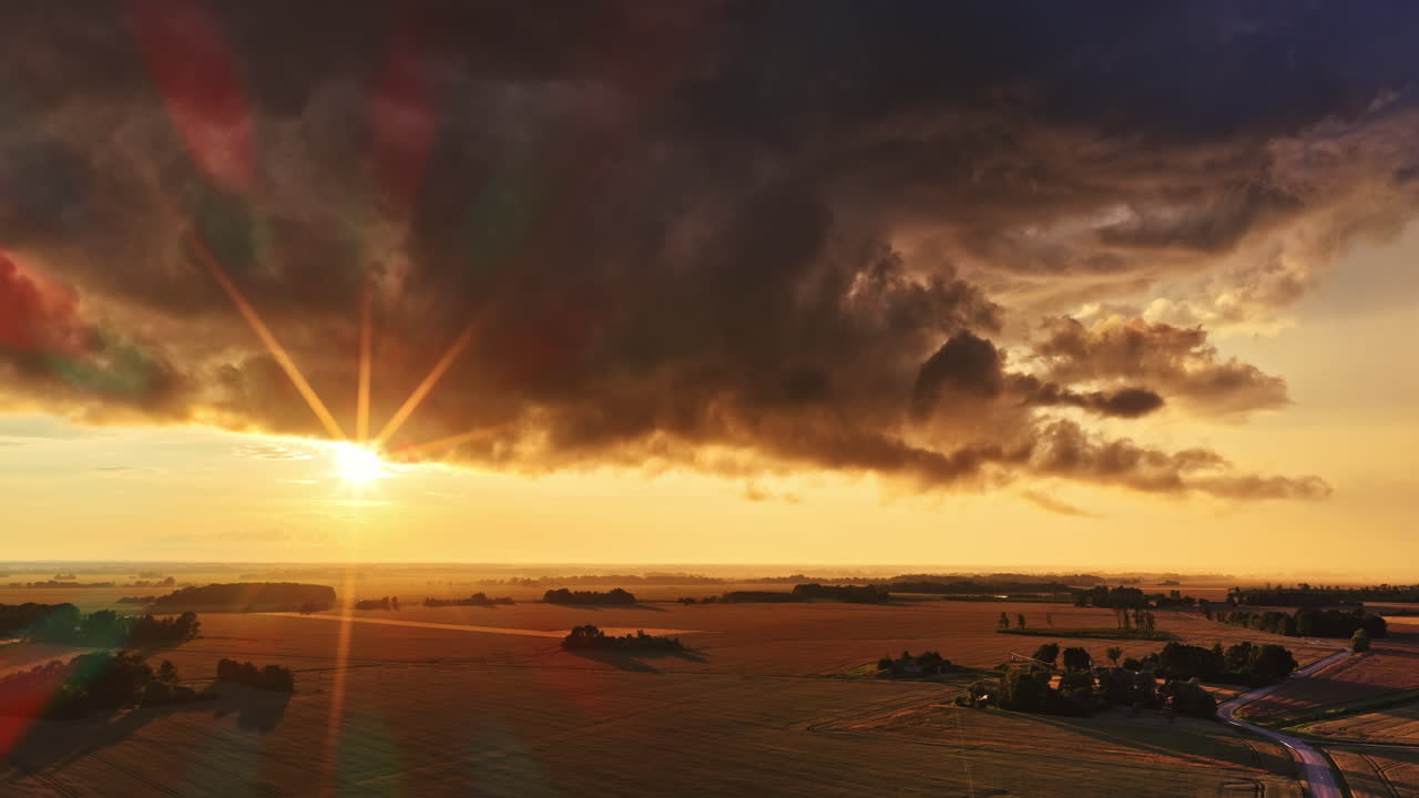 Sunrise sun rays from thick layer of rain clouds, low level gray color over rural landscape