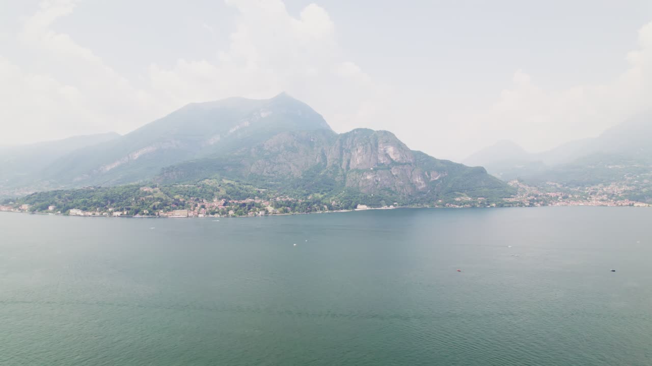 Filmato aereo cinematografico realizzato con drone sopra il Lago di Como, in Italia, con montagne nuvolose sullo sfondo che creano una scena suggestiva e carica di atmosfera