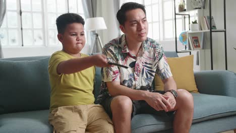 father and his son are watching tv while spending time together at home